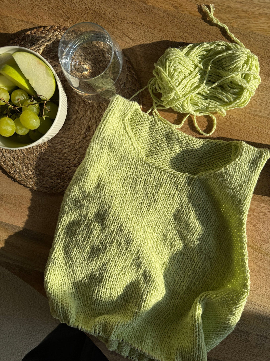 A lime green hand knitted slipover laid flat on a wooden table next to a skein of matching yarn