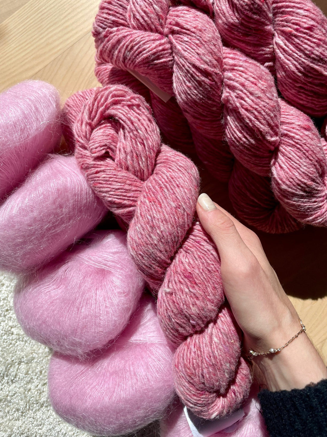 A hand holding a skein of pink tweed yarn next to skeins of pink mohair, a favorite yarn combination for knitting